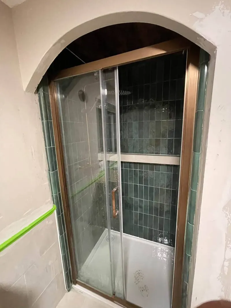 Finished arched shower alcove by OJP Plumbing with deep green tiles, bronze sliding enclosure and rainfall shower