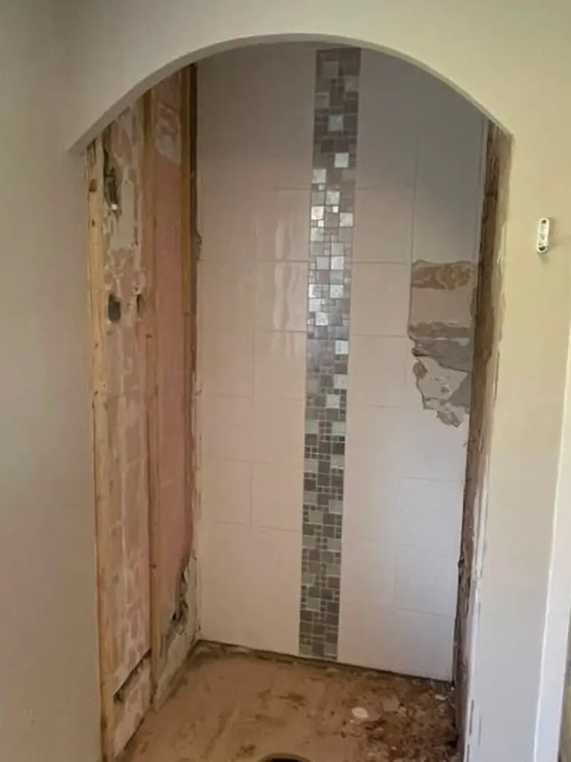 Shower alcove before: old tiles, damaged boards and the old tray removed, leaving bare timber and a waste hole